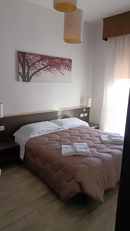 Camera moderna dell'Hotel Eden a Vignola con opere floreali rosa, trapunta marrone e illuminazione a sospensione.