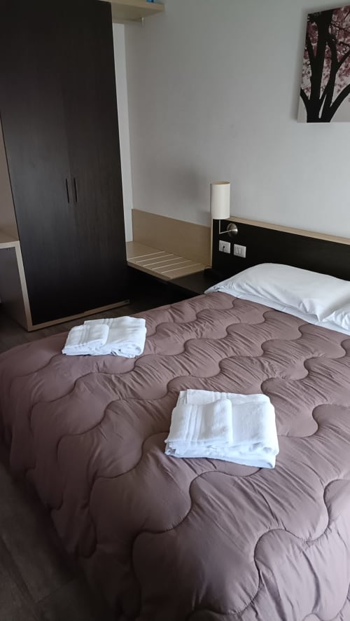 Camera moderna all'Hotel Eden di Vignola con letto trapuntato marrone, guardaroba nero e biancheria da letto bianca