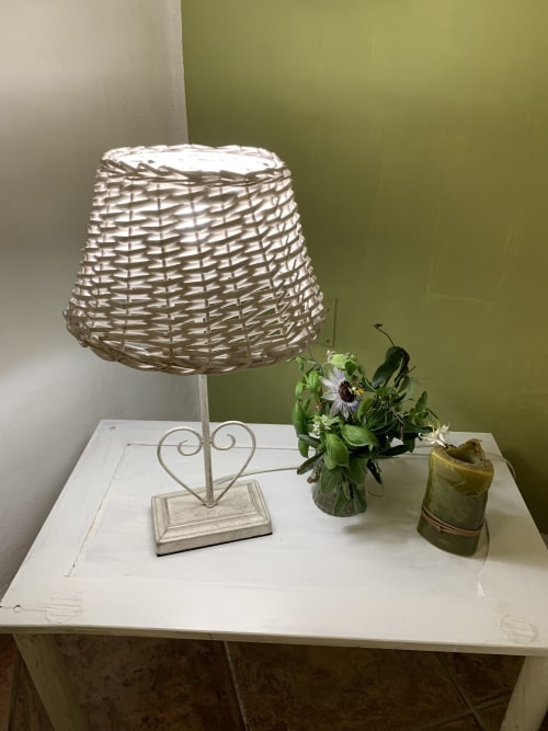 Lampada da comodino con paralume intrecciato e base a forma di cuore, fiori freschi in vaso su tavolo bianco all'Agriturismo Il Pomo d'oro