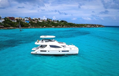 White luxury yacht anchored in turquoise Caribbean waters off Tulum with beachfront homes on cliff