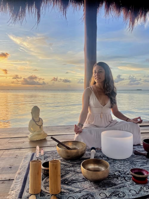Woman in white dress meditating at sunset beach setup with singing bowls in Tulum