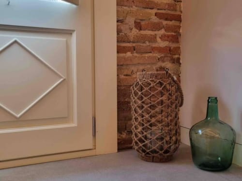 Detalle decorativo del apartamento turístico en Blanes, Costa Brava, mostrando una pared de ladrillo visto junto a una linterna de cuerda y un jarrón de vidrio verde. Esta combinación de elementos rústicos añade un toque de encanto y autenticidad al espacio.