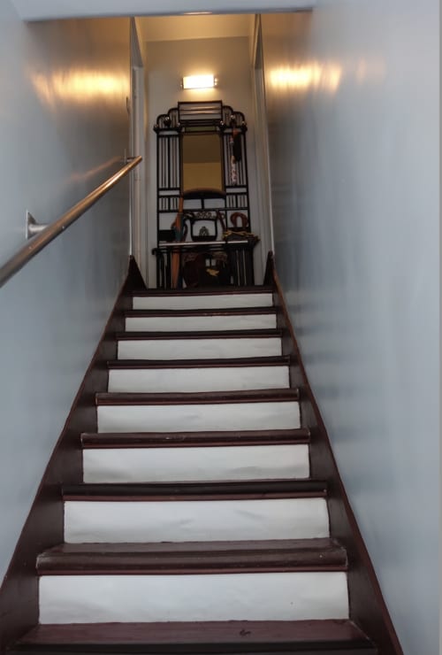 Escalier en bois de la Maison 1850 Paris, un gîte montmartrois, menant à l'étage supérieur aux murs blancs