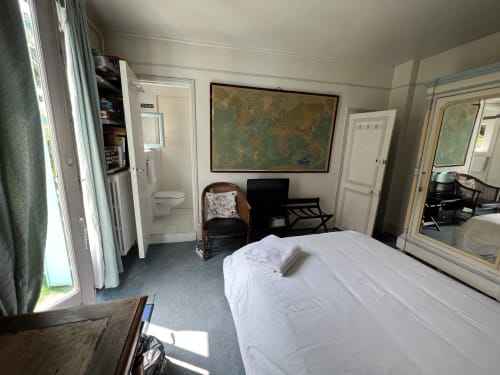 Chambre de Gaspard à la Maison 1850 Paris avec vue sur le jardin, lit, fauteuil en osier et mappemonde au mur