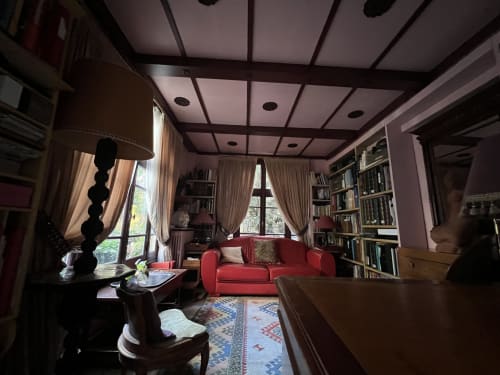Élégante bibliothèque de villa parisienne avec canapé rouge, étagères, plafond à caissons et vue sur le jardin à Maison 1850