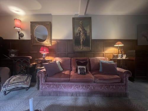 Élégant salon de villa parisienne avec canapé bourgogne, tableaux de portraits, miroirs ornementés et éclairage ambiant chez Maison 1850