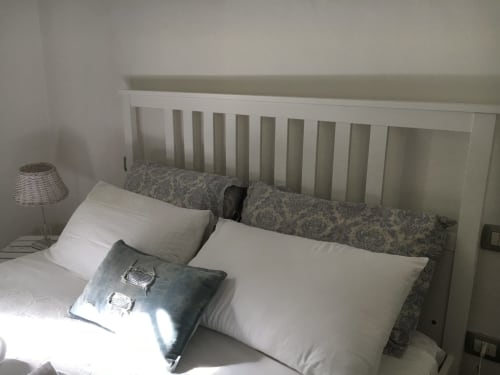 Letto in legno bianco con cuscini grigio patterned e biancheria bianca in una cottage con vista giardino presso Agriturismo Il Pomo d'oro, Assemini
