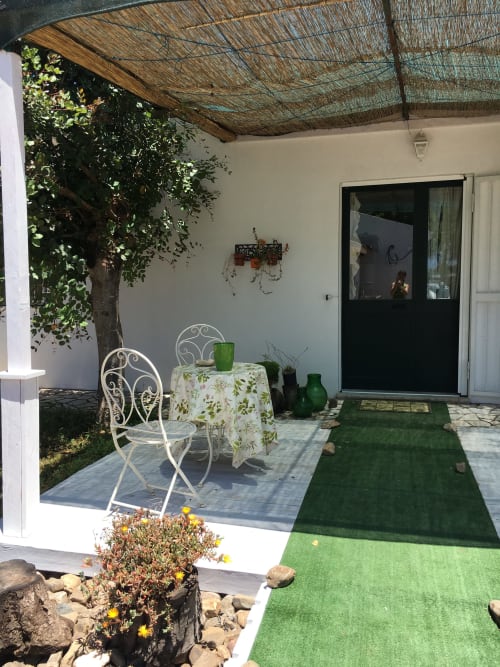 Patio ombreggiato dell'agriturismo Il Pomo d'oro con sedie in ferro battuto bianco, tavolo da pranzo e prato sintetico