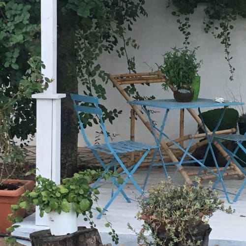 Sedie da campeggio blu e tavolo in legno sulla terrazza del giardino dell'Agriturismo Il Pomo d'oro, circondati da piante in vaso