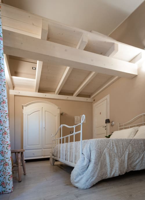 Camera luminosa con letto in metallo bianco, travi in legno a vista e pareti color crema presso Agriturismo Il Pomo d'oro