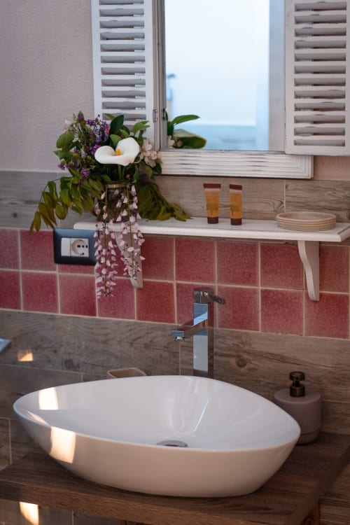 Bagno moderno presso Agriturismo Il Pomo d'oro con lavabo ovale bianco, piastrelle rosse, mobile in legno e composizione floreale