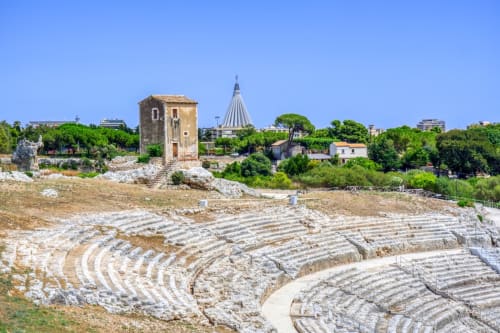 Rovine dell'anfiteatro greco antico a Siracusa con torre medievale e cupola della chiesa sullo sfondo