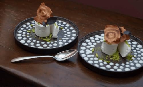 Two elegant plated desserts at Three Little Pigs hotel featuring pistachio mousse, crispy tuile, and micro garnish on dark