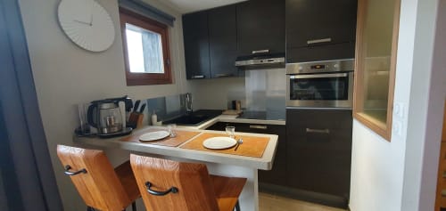 Cuisine moderne avec meubles noirs, îlot blanc et chaises en bois à la Résidence Le Pacha, Courchevel