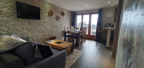 Appartement à Courchevel aux murs en pierre, table à manger, canapé sombre, TV écran plat et balcon vue montagne