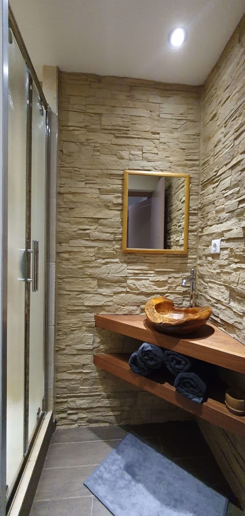 Salle de bain moderne à la Résidence Le Pacha Courchevel avec murs en pierre, meuble vasque en bois et sèche-serviettes chauffant