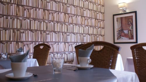 Salle à manger de l'hôtel Be Le Touquet avec chaises en rotin, nappes blanches et bibliothèque du sol au plafond