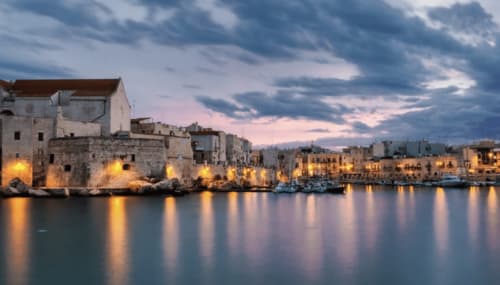 Edifici storici del lungomare di Bari al tramonto, con luci dorate riflesse nell'acqua tranquilla