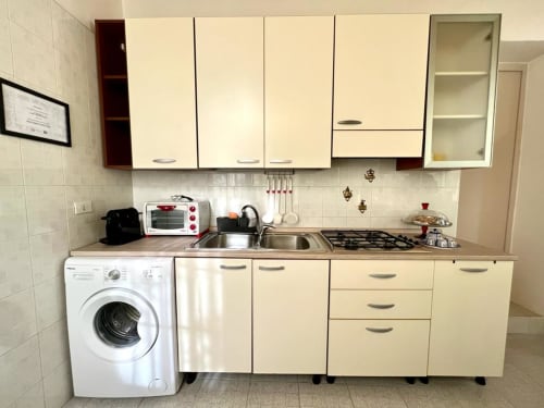 Cucina moderna nella villa Newhouse di Bari con mobili color crema, lavello in acciaio inox, piano cottura a gas e lavatrice.