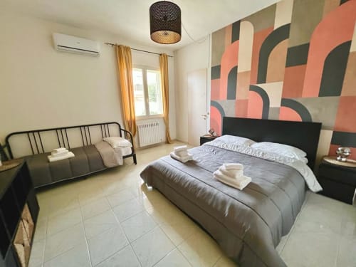 Camera da letto moderna della villa Newhouse Bari con letto matrimoniale, arte geometrica alle pareti, aria condizionata, accesso al balcone e arredi contemporanei