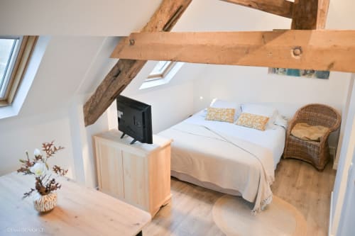 Chambre lumineuse avec poutres apparentes, lit queen-size, TV, fauteuil rotin et puits de lumière à Villa République Normandie, Caen