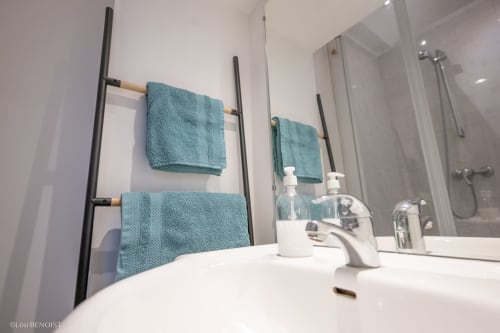 Salle de bain moderne à la Villa République Normandie à Caen avec lavabo blanc, serviettes turquoise sur porte-serviettes noir et douche vitrée