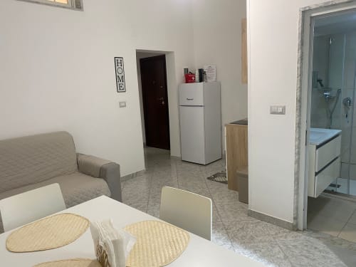 Moderno monolocale a Bari con zona pranzo, frigorifero, divano grigio e ingresso bagno visibile