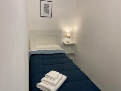 Camera moderna dell'appartamento Newhouse a Bari con testiera bianca, biancheria blu navy, asciugamani freschi, lampada comodino e motivazionale
