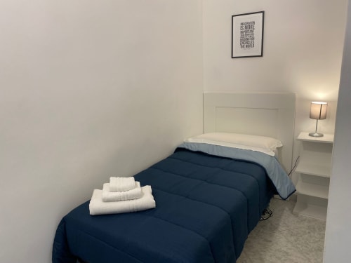 Camera da letto dell'appartamento Newhouse a Bari con due letti singoli, testiere bianche, coperte blu scuro e lampada comodino