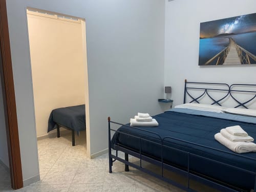 Camera luminosa all'apartamento Newhouse di Bari con letti singoli, biancheria blu scuro, asciugamani bianchi e foto della passeggiata sul mare