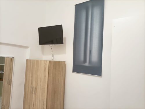 Camera moderna di Newhouse Bari con TV a parete sopra l'armadio in legno e tende grigie