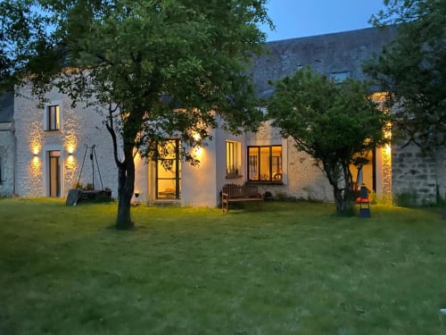 Le gîte La Ferme du Châtaignier au crépuscule, maison de pierre chaleureusement éclairée, pelouse entretenue et arbres matures à Boissy-le-Sec