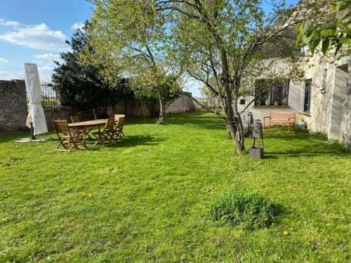 Jardin spacieux avec mobilier en bois, arbres fruitiers et bâtisses en pierre à La Ferme du Châtaignier en Essonne, barecue, soirée, farniente.