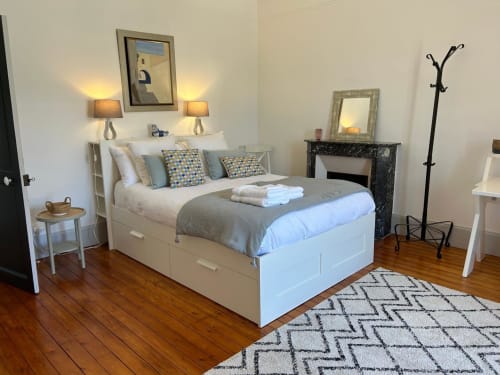 Chambre élégante avec lit blanc de rangement, accents bleus, cheminée et parquet à La Ferme du Châtaignier près de Paris