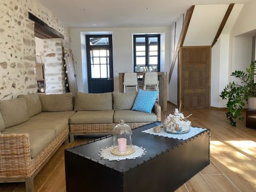 Élégant séjour du gîte La Ferme du Châtaignier en Essonne avec murs de pierre, canapé en osier et table basse noire