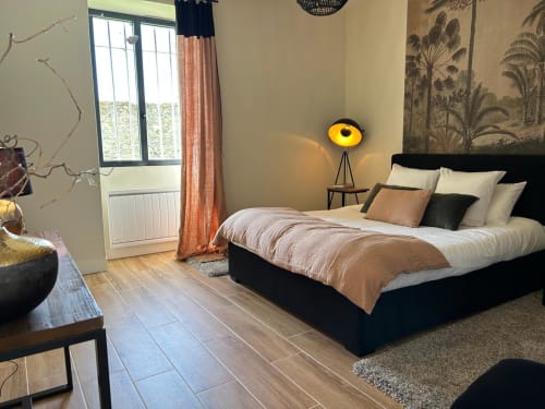 Chambre élégante à La Ferme du Châtaignier en Essonne : lit noir, lampe jaune et vue sur le jardin