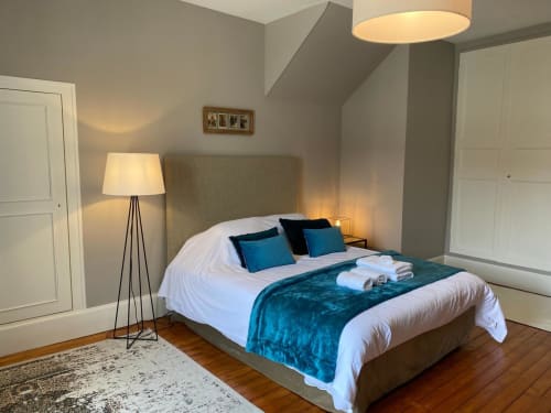 Chambre élégante à La Ferme du Châtaignier avec tête de lit beige, plaid velours bleu canard, literie blanche et lampadaire moderne
