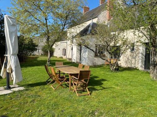 Espace de restauration extérieur du gîte La Ferme du Châtaignier avec table en bois, chaises, parasol et jardin luxuriant près de Paris