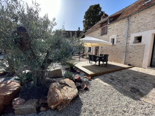 Terrasse en pierre avec coin repas, parasol, oliviers et jardin de gravier à La Ferme du Châtaignier en Essonne