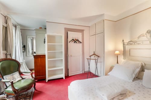 Chambre Rita à Maison 1850 Paris avec lit blanc, fauteuil vert, tapis rouge et armoire, vue sur le jardin