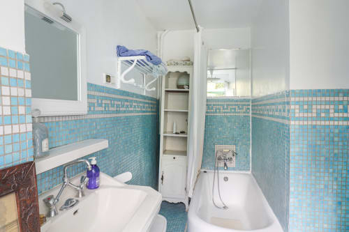 Salle de bains lumineuse à Maison 1850 Paris avec carrelage turquoise, lavabo blanc, baignoire et miroir dans cette maison d'hôtes à Montmartre.