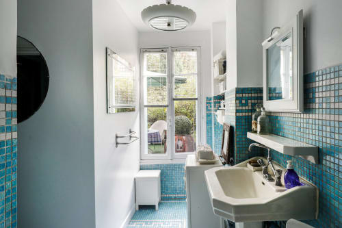 Salle de bain de la chambre de Rita à la Maison 1850 Paris avec carreaux de mosaïque turquoise, lavabo blanc et portes donnant sur le jardin