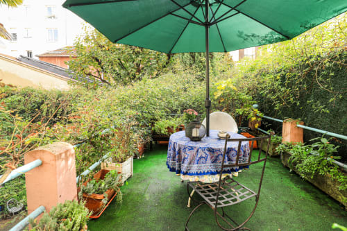 Terrasse de jardin privé à la Maison 1850 Paris avec parasol vert, table ronde et verdure luxuriante