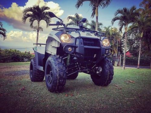VTT modifié garé sur l'herbe à Kaz A Bibi à Sainte-Rose, Guadeloupe, entouré de palmiers et de paysages tropicaux.