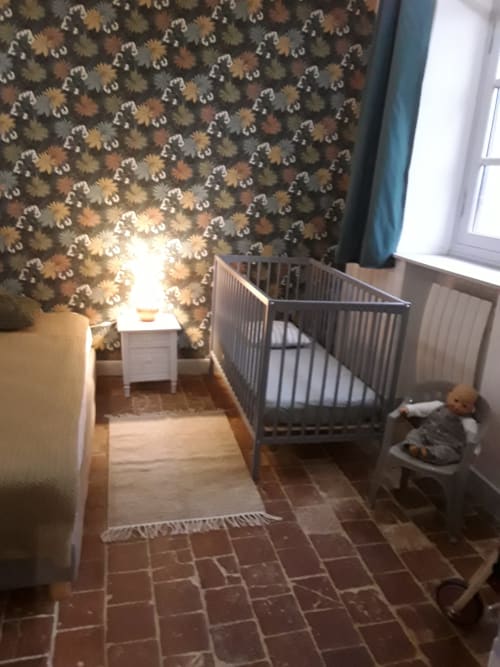 Habitación infantil de la Château De Clusors con papel pintado estampado, cuna, lámpara y suelo de baldosas de terracota