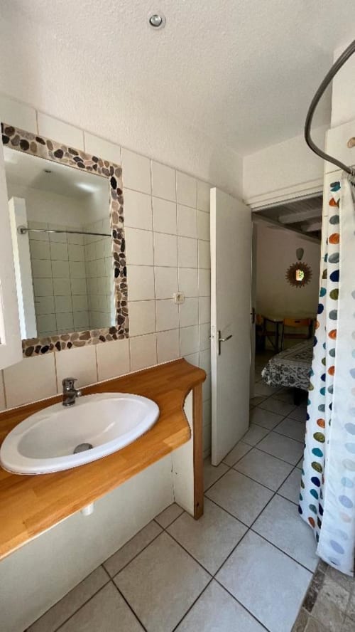 Salle de bains du studio Le Maquis Plage avec vanité en bois, lavabo rond, carrelage mural et rideau de douche coloré à Poggio-Mezzana