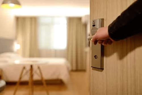 Main ouvrant la porte d'une chambre moderne à La Conciergerie du Cap Corse à Centuri avec lit et fenêtres