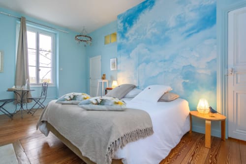 Chambre de couleur bleue traversante avec accès balcon et papier peint avec des nuages. Sol en parquet