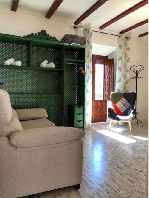 Modern studio room with green shelving, beige armchair, patterned chair, wooden beams, and wood flooring in Almagro hotel