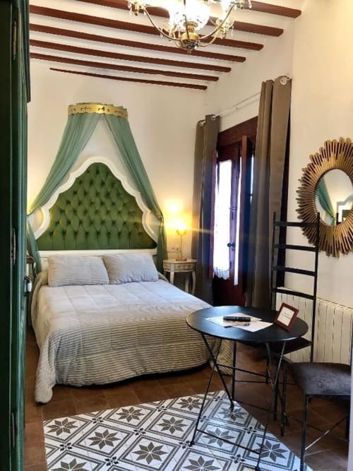 Elegant bedroom at Complejo Turístico Retiro del Teatro with green tufted canopy bed, wooden beamed ceiling, and city views
